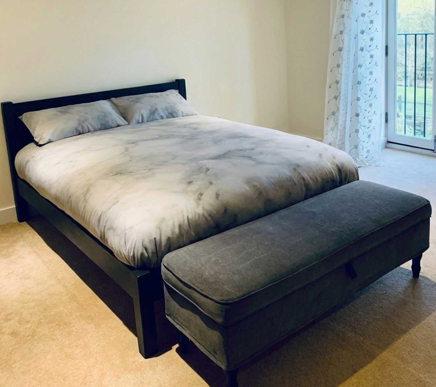 Ein schwarzes Holzbettgestell schafft einen starken Fokuspunkt in einem schwarz-cremefarbenen Schlafzimmer und bietet einen Kontrast zu hellen Wänden und Bettwäsche. Es ist eine einfache Möglichkeit, Struktur einzuführen, ohne auf auffällige Dekoration angewiesen zu sein.